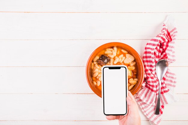 Photo gratuite main avec mobile sur la table avec la plaque alimentaire