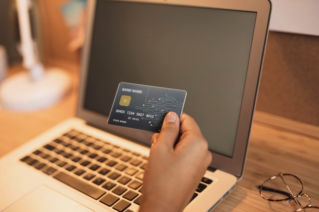 Main montrant une carte de crédit à côté d'un ordinateur portable