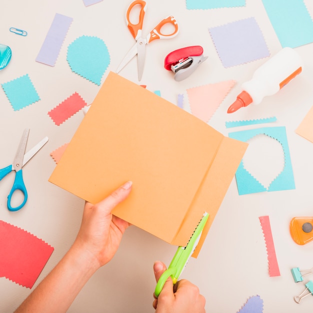 Main de la personne coupe le papier coloré sur les fournitures scolaires sur la table