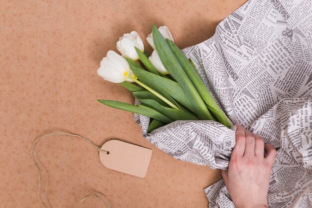 Main de la personne, emballage de fleurs de tulipes blanches dans un journal avec étiquette de prix sur fond marron