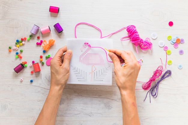 Une main de personne fait de la broderie avec des éléments décoratifs sur un fond texturé