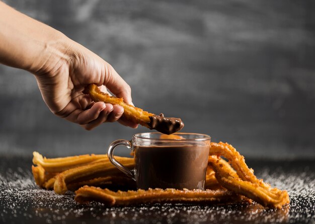 Main plongeant un churros frit en vue de face de chocolat