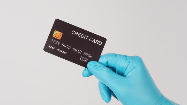 Main portant un gant médical et tenant une carte de crédit noire isolée sur fond blanc. main d'homme asiatique.