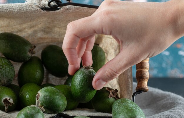 Main prenant un feijoa du panier sur une nappe grise