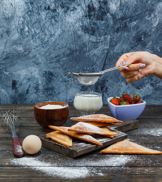 Main saupoudrer de farine sur gaufre sur planche de bois