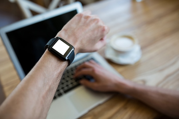 Main smartwatch portant l&#39;aide d&#39;un ordinateur portable dans un café