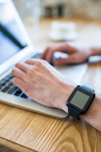 Main avec smartwatch en utilisant un ordinateur portable dans un café