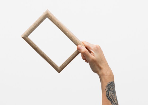 Main avec tatouage tenant un cadre en bois