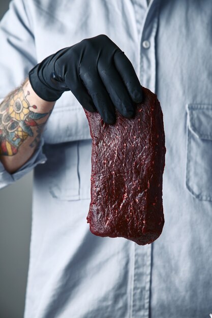 La main tatouée dans un gant noir détient un morceau de steak de luxe dans l'air