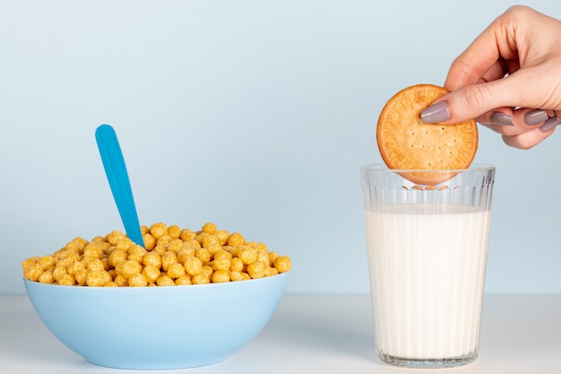 Main tenant un biscuit au-dessus du lait et un bol de céréales