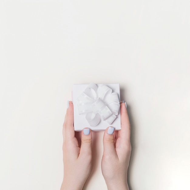 Main tenant une boîte cadeau décorée de ruban blanc sur fond blanc
