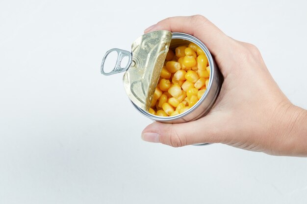 Main tenant une boîte de conserve de maïs sucré bouilli.