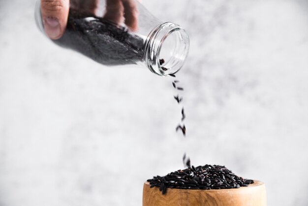 Main tenant une bouteille avec du riz noir près du bol