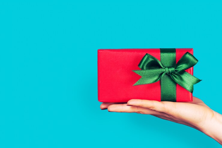 Photo gratuit une main tenant un cadeau rouge avec arc vert
