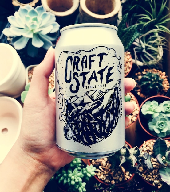 Main tenant la canette de bière de l&#39;état de l&#39;artisanat avec fond de plantes d&#39;intérieur