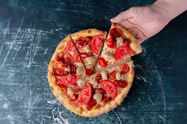 Main tenant une délicieuse pizza au poulet aux tomates sur marbre.