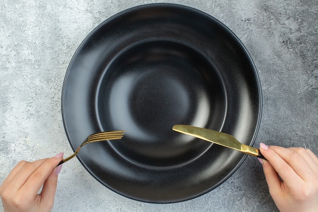 Main tenant une fourchette et un couteau élégants sur de la vaisselle noire sur une surface de glace grise isolée avec un espace libre