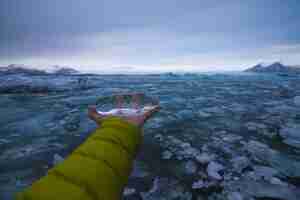 Photo gratuite main tenant la glace avec une mer gelée sous un ciel nuageux en islande sur l'arrière-plan