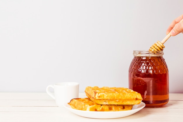 Main tenant une louche de miel de pot de miel et un délicieux petit déjeuner sur la table