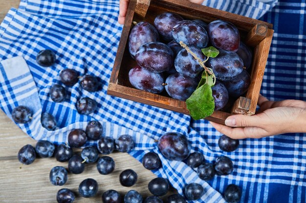 Photo gratuite main tenant un panier en bois de prunes de jardin sur table en bois.