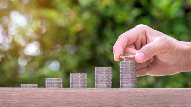 Main tenant une pièce de monnaie et une pile d'argent sur une table en bois Concept de fonds de pension