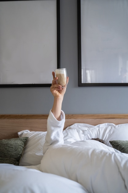 Main tenant une tasse de café à la maison au lit