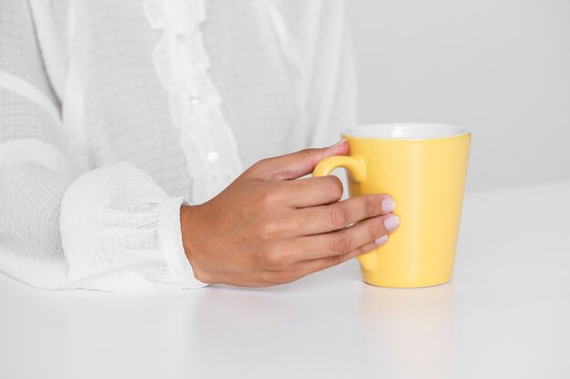 Main tenant une tasse jaune sur une table