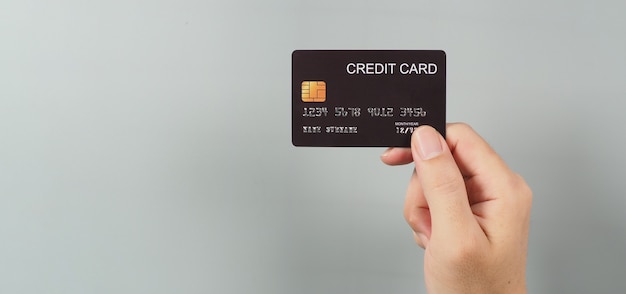 La main tient une carte de crédit noire isolée sur fond gris.