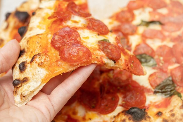 La main tient une tranche de pizza italienne parfumée avec pepperoni, fromage, basilic