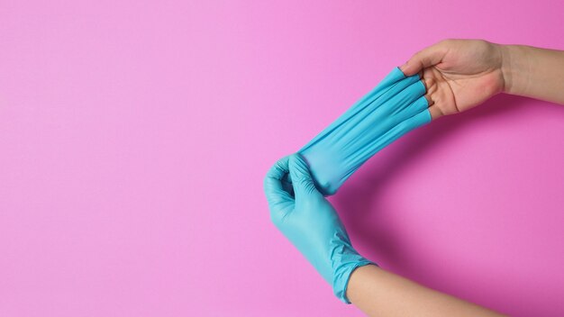 La main tire des gants en caoutchouc ou un gant en latex bleu sur fond rose
