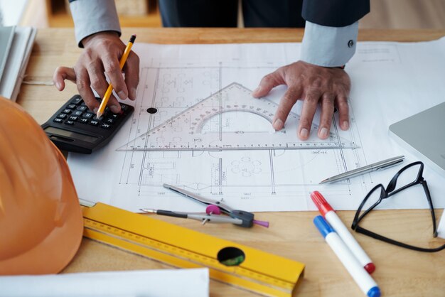 Mains d'un architecte masculin méconnaissable travaillant sur un dessin technique et utilisant une calculatrice