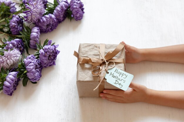 Mains de bébé et coffret cadeau à maman pour la fête des mères, sur fond blanc avec des fleurs de chrysanthème fraîches.