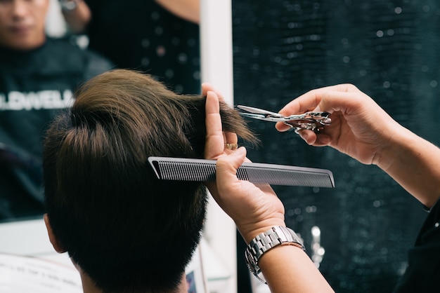Mains d'un coiffeur méconnaissable coupant les cheveux d'un client masculin dans un salon