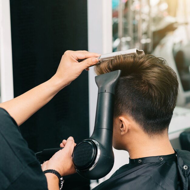 Mains d'un coiffeur méconnaissable donnant à un client masculin un blowdry avec un sèche-cheveux et un peigne