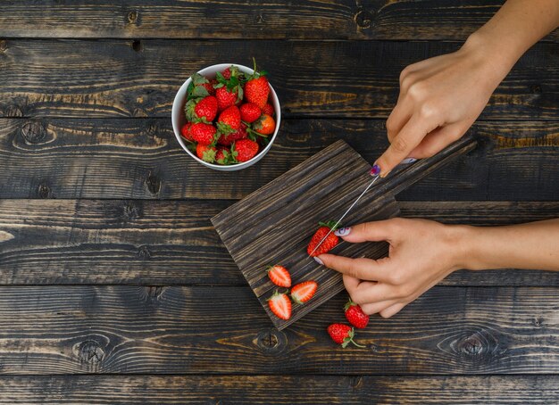 Mains coupant les fraises avec un couteau sur planche de bois