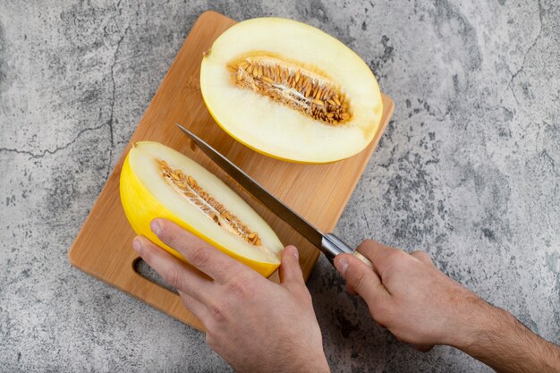 Mains coupant le melon jaune frais sur une planche à découper en bois.