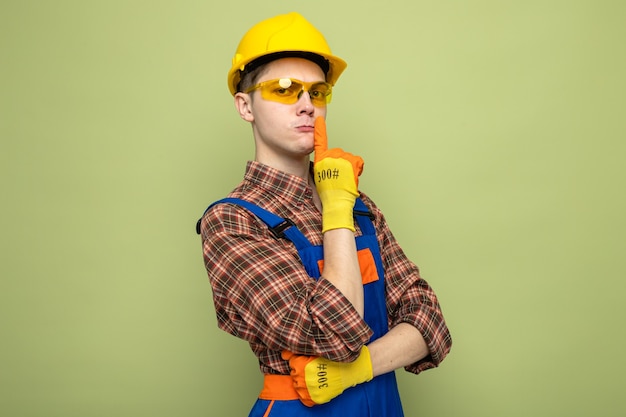 Mains croisées strictes montrant un geste de silence jeune constructeur masculin portant des uniformes et des gants avec des lunettes