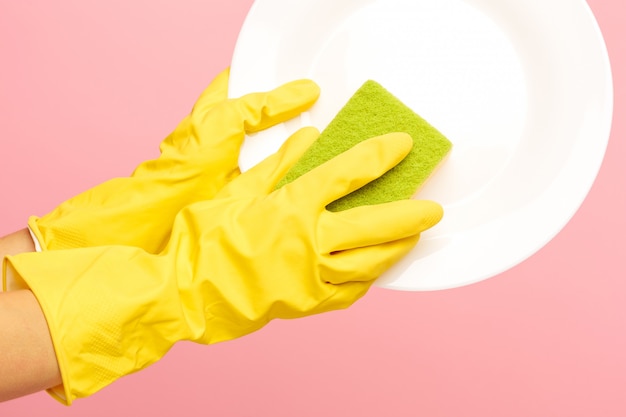 Mains dans des gants de protection jaunes, laver une assiette