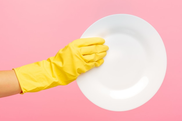 Mains dans des gants de protection jaunes, laver une assiette