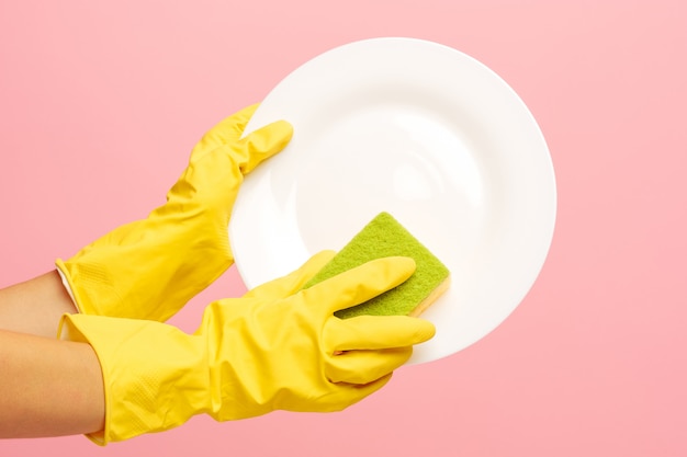 Mains dans des gants de protection jaunes, laver une assiette