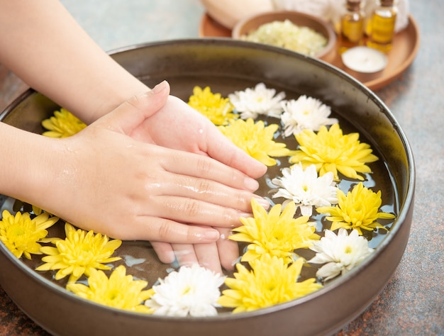 Mains féminines et bol d'eau de spa avec des fleurs, gros plan. Spa des mains.