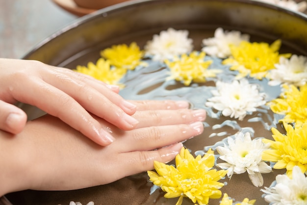 Mains féminines et bol d'eau de spa avec des fleurs, gros plan. Spa des mains.