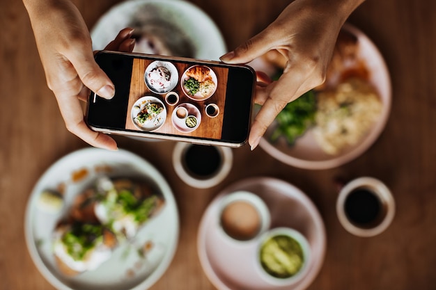 Mains féminines bronzées tenant le smartphone et prendre des photos de l'assiette avec repas