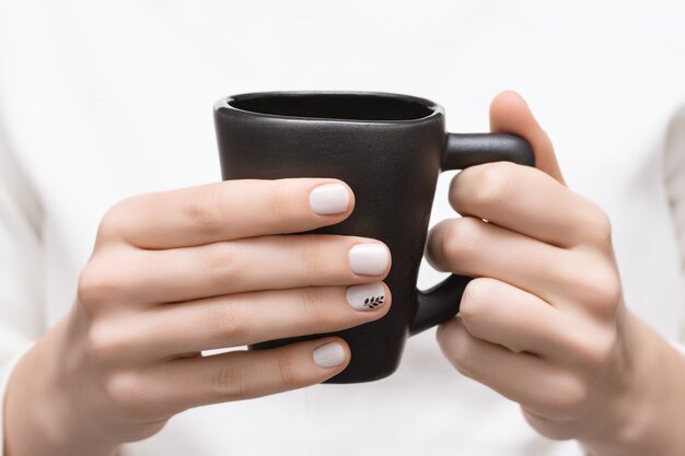 Mains féminines avec un design d'ongle blanc tenant une tasse noire.