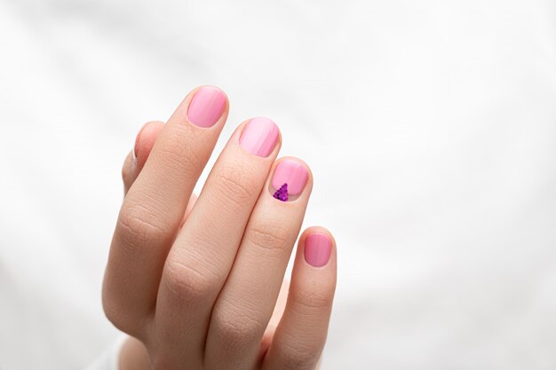 Mains féminines avec des ongles roses sur fond de tissu blanc.
