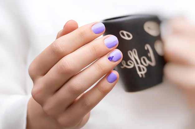 Mains féminines avec des ongles violets tenant une tasse noire.