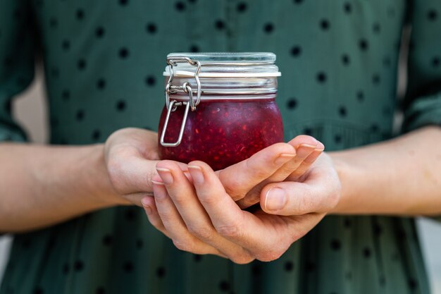 Mains féminines tenant une confiture de framboises crues vegan maison dans un bocal en verre