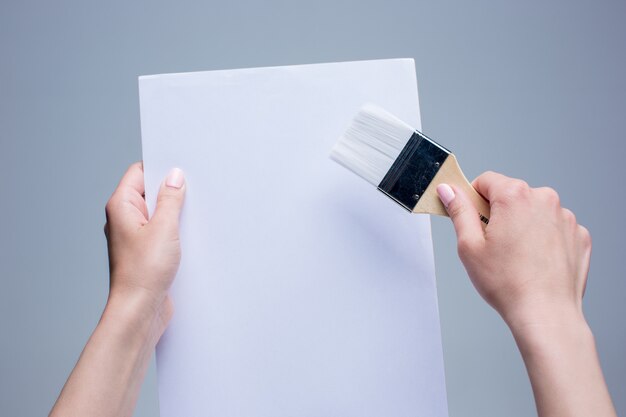 Les mains féminines tenant un pinceau sur toile blanche