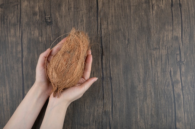 Mains féminines tenant une seule noix de coco mûre sur une surface en bois