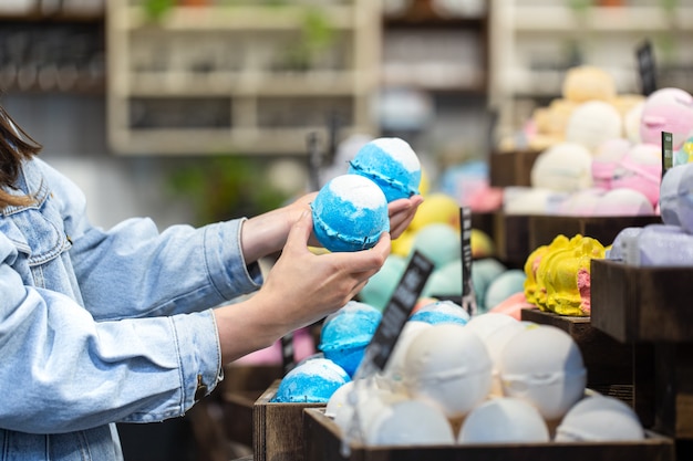 Des mains féminines tiennent des bombes de bain lumineuses dans un magasin de cosmétiques. Concept de soins du corps.